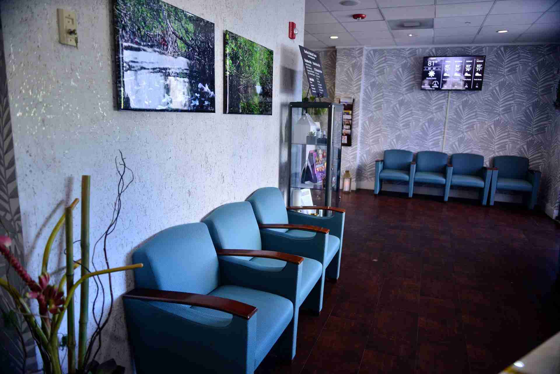 Waiting room with blue chairs, white counter and paintings on the white wall